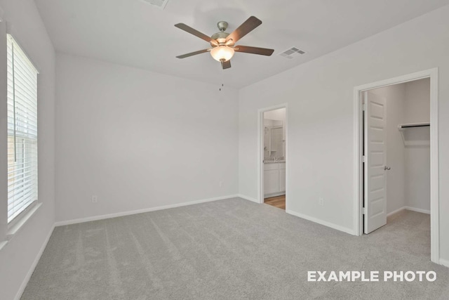 unfurnished bedroom with ceiling fan, multiple windows, a walk in closet, and light colored carpet