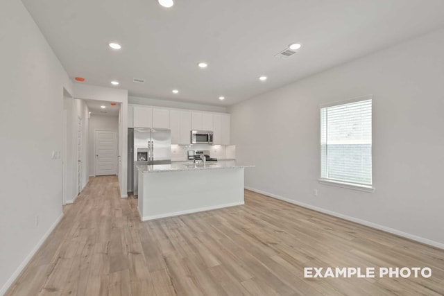 kitchen featuring appliances with stainless steel finishes, white cabinetry, light hardwood / wood-style flooring, and a kitchen island with sink