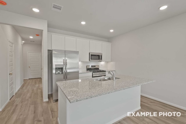 kitchen with white cabinetry, light stone countertops, light hardwood / wood-style flooring, appliances with stainless steel finishes, and tasteful backsplash