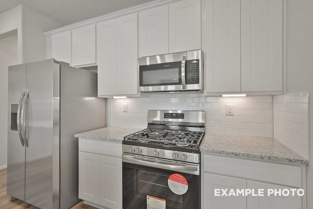 kitchen featuring light wood-type flooring, appliances with stainless steel finishes, white cabinets, light stone counters, and backsplash