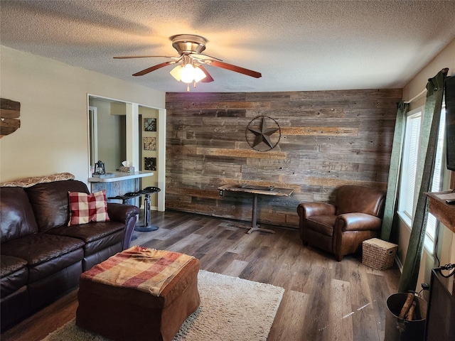 living room with wood walls, ceiling fan, wood-type flooring, and a textured ceiling