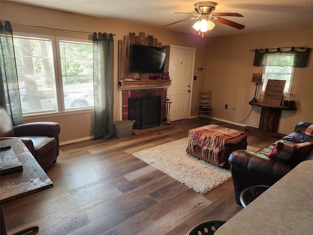 living room featuring a textured ceiling, hardwood / wood-style flooring, a brick fireplace, and ceiling fan