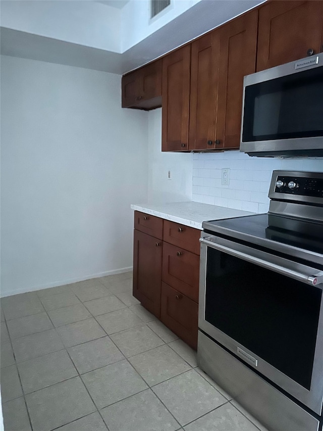 kitchen with dark brown cabinets, light tile patterned flooring, stainless steel appliances, and decorative backsplash