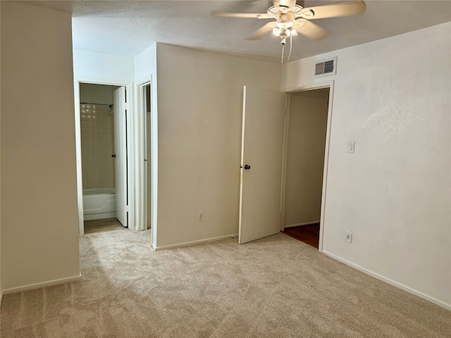 unfurnished bedroom featuring ensuite bath, light carpet, ceiling fan, and a textured ceiling