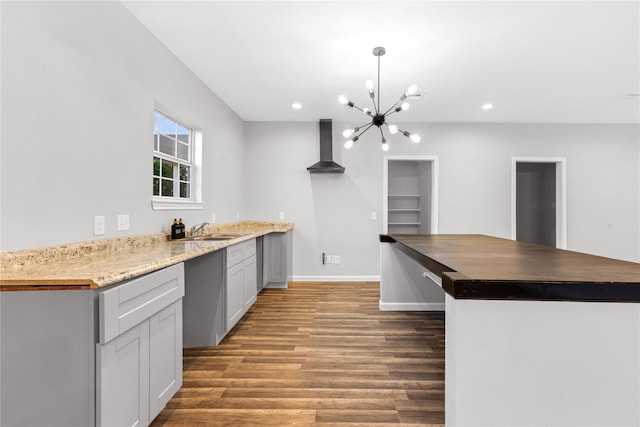 kitchen with pendant lighting, wall chimney range hood, sink, kitchen peninsula, and dark stone counters