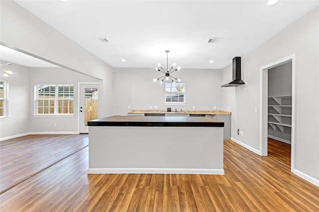 kitchen featuring wall chimney exhaust hood, a center island, hanging light fixtures, light hardwood / wood-style flooring, and a notable chandelier