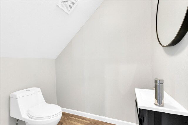 bathroom with vanity, toilet, hardwood / wood-style flooring, and lofted ceiling