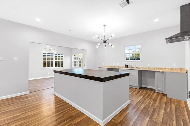 kitchen featuring wall chimney exhaust hood, hardwood / wood-style flooring, and an inviting chandelier