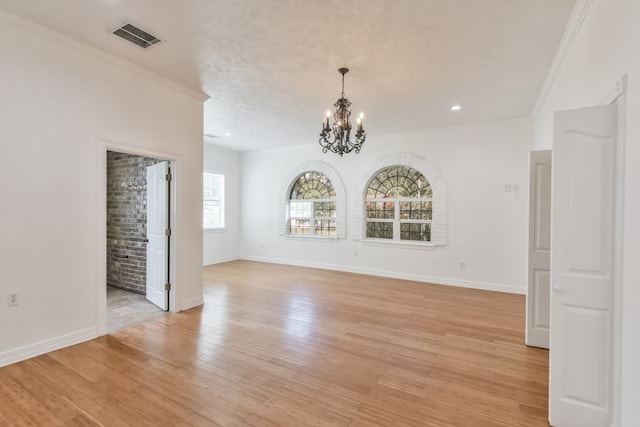 spare room featuring a chandelier, light hardwood / wood-style flooring, a textured ceiling, and ornamental molding