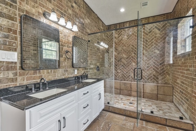 bathroom with tile flooring, double sink, a shower with shower door, brick wall, and large vanity