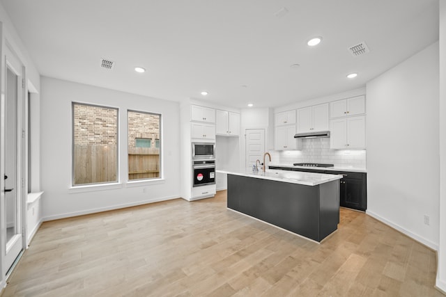 kitchen with a kitchen island with sink, white cabinetry, decorative backsplash, appliances with stainless steel finishes, and light hardwood / wood-style floors