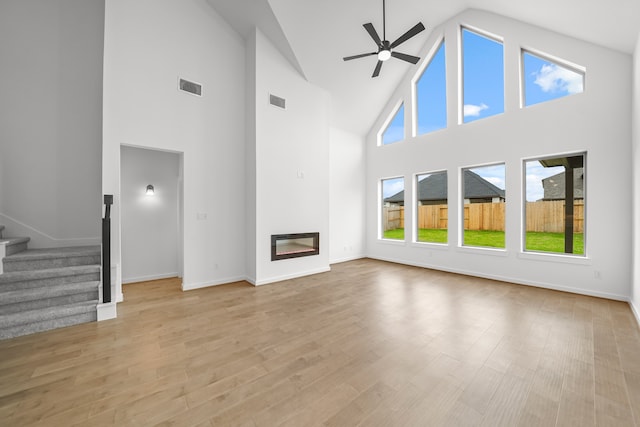 unfurnished living room with light hardwood / wood-style flooring, ceiling fan, and high vaulted ceiling