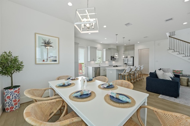 dining space featuring sink, light hardwood / wood-style floors, and an inviting chandelier