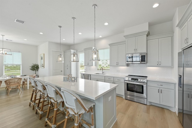 kitchen with decorative backsplash, appliances with stainless steel finishes, a kitchen island, hanging light fixtures, and a breakfast bar area