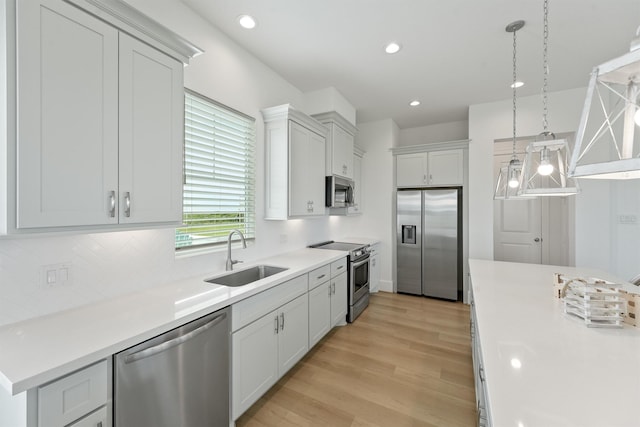 kitchen featuring white cabinets, hanging light fixtures, sink, appliances with stainless steel finishes, and light hardwood / wood-style floors