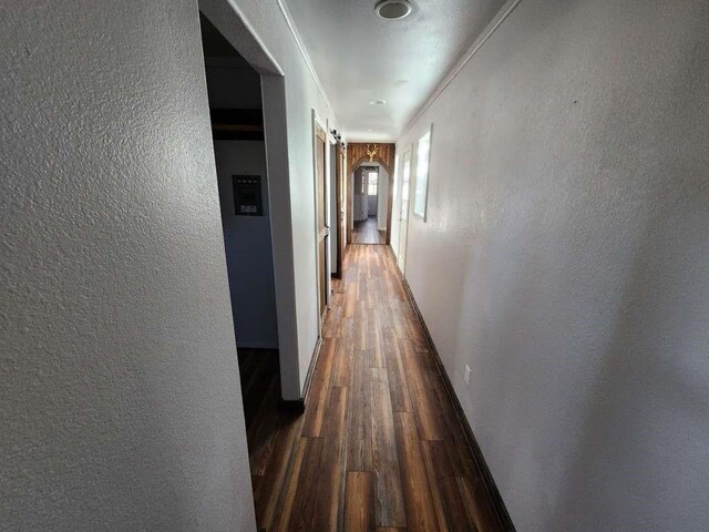 hallway featuring dark wood-type flooring, ornamental molding, and a barn door