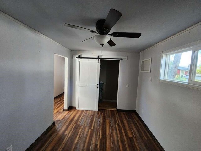 unfurnished bedroom featuring dark hardwood / wood-style flooring, ornamental molding, a barn door, and ceiling fan