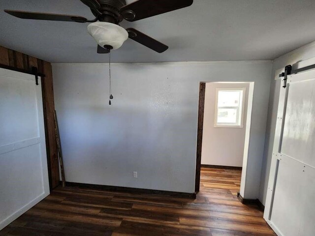 unfurnished room featuring ceiling fan, a barn door, and dark hardwood / wood-style flooring