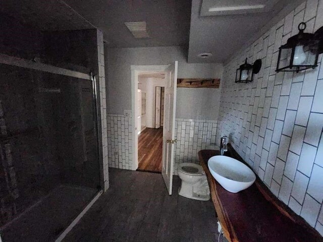 bathroom featuring tile walls, hardwood / wood-style flooring, a shower with door, and toilet