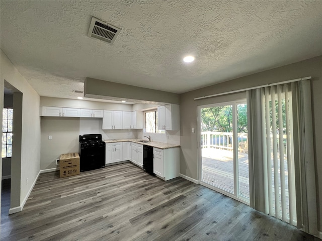 kitchen featuring a textured ceiling, hardwood / wood-style floors, white cabinets, and black appliances