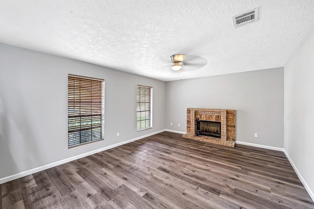 unfurnished living room featuring dark wood-type flooring, ceiling fan, a textured ceiling, and a brick fireplace