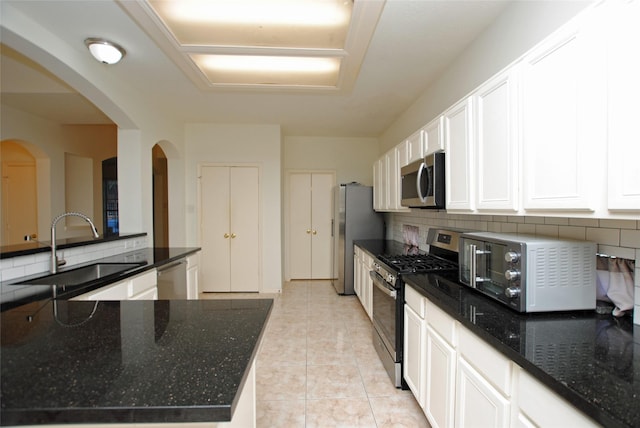 kitchen with appliances with stainless steel finishes, tasteful backsplash, dark stone counters, sink, and white cabinetry