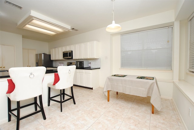 kitchen with appliances with stainless steel finishes, backsplash, a breakfast bar, white cabinetry, and hanging light fixtures