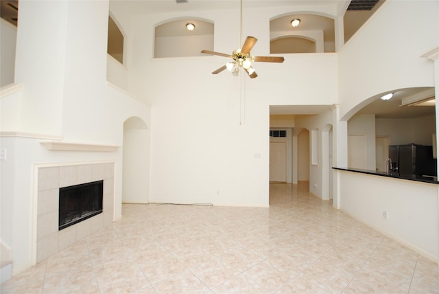 unfurnished living room with light tile patterned flooring, a high ceiling, ceiling fan, and a tiled fireplace