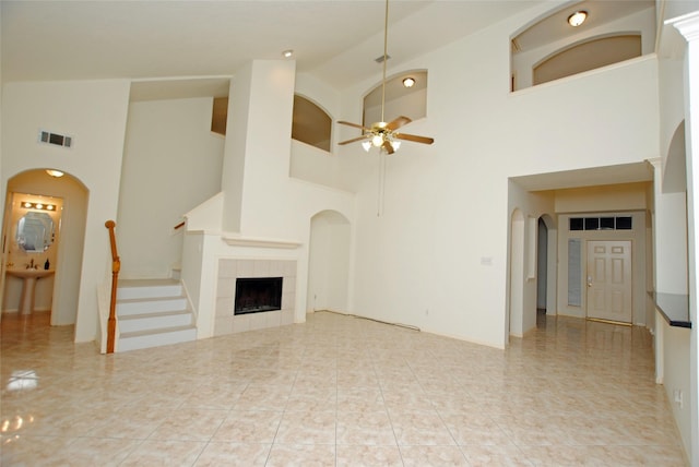 unfurnished living room with light tile patterned floors, high vaulted ceiling, ceiling fan, and a tiled fireplace