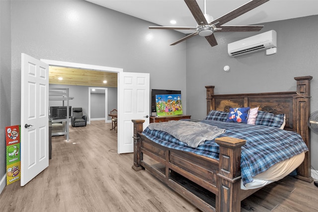 bedroom with a wall mounted AC, light wood-type flooring, ceiling fan, and a towering ceiling