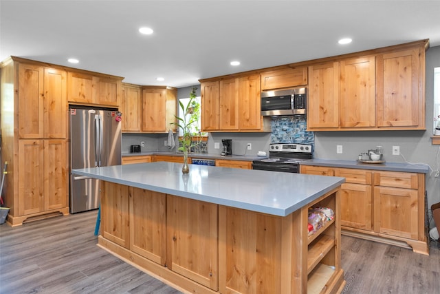 kitchen with appliances with stainless steel finishes, light hardwood / wood-style flooring, a center island, and backsplash