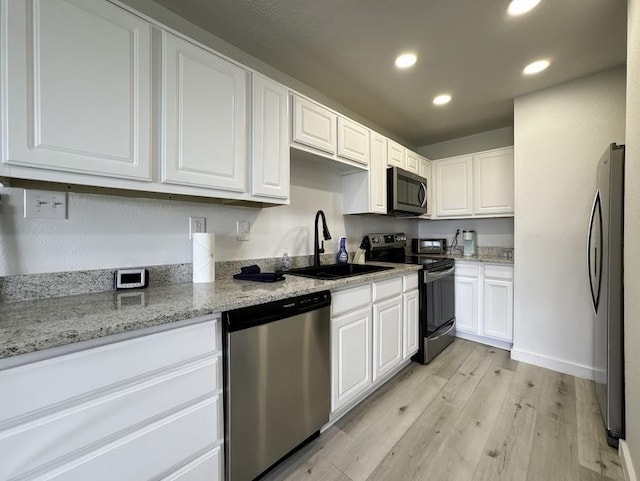 kitchen with white cabinets, light stone countertops, light wood-type flooring, and stainless steel appliances