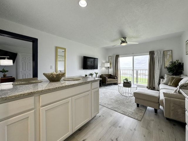 living room with a textured ceiling, light hardwood / wood-style floors, and ceiling fan