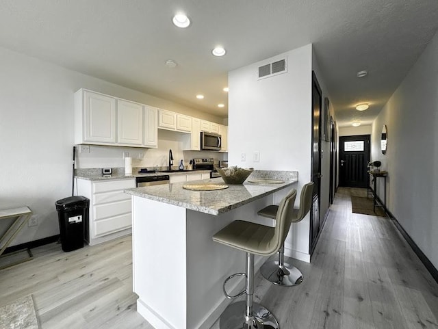 kitchen with kitchen peninsula, appliances with stainless steel finishes, light stone countertops, a kitchen breakfast bar, and white cabinets