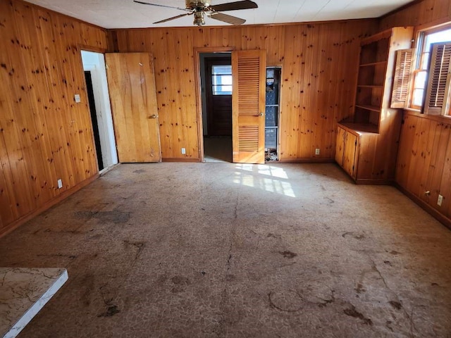 carpeted spare room with wood walls, plenty of natural light, and ceiling fan