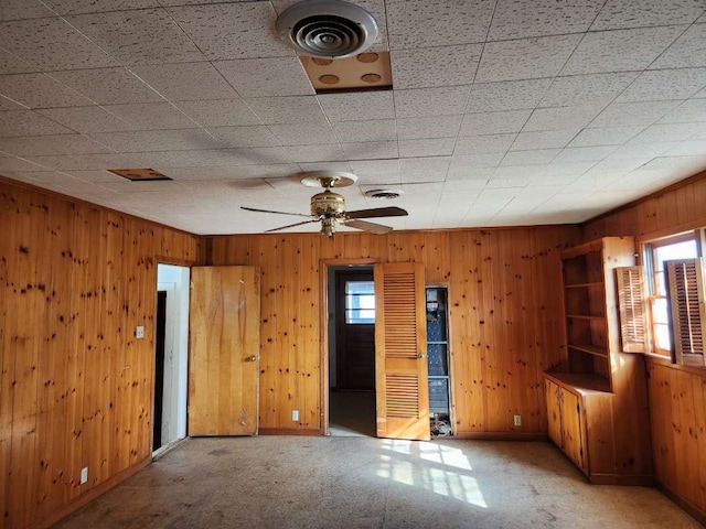 carpeted empty room featuring a healthy amount of sunlight, wood walls, and ceiling fan