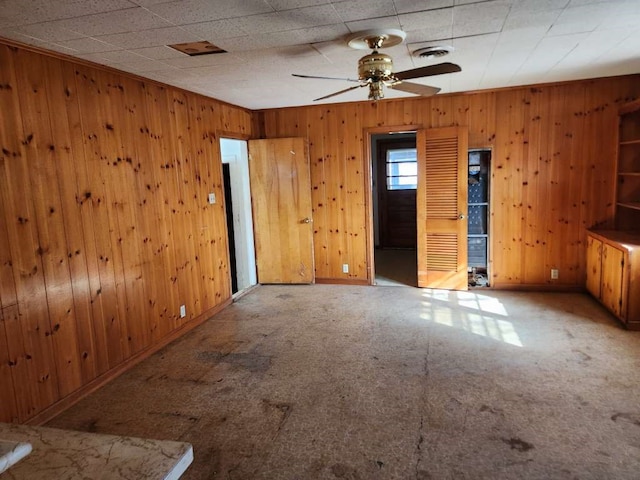 unfurnished room featuring carpet, ceiling fan, and wood walls