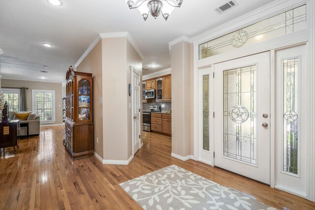 foyer with crown molding, light hardwood / wood-style floors, and a notable chandelier