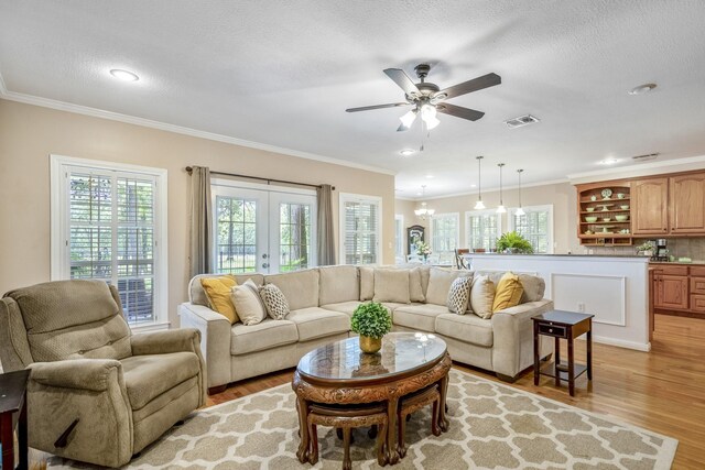 living room with a textured ceiling, ceiling fan with notable chandelier, light wood-type flooring, and ornamental molding