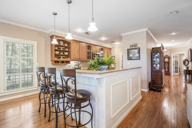 kitchen with light stone counters, pendant lighting, light hardwood / wood-style floors, a breakfast bar area, and ornamental molding