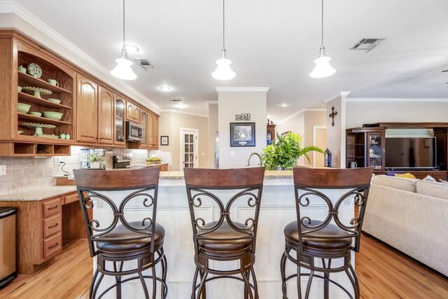 kitchen with backsplash, a kitchen breakfast bar, crown molding, decorative light fixtures, and stainless steel appliances