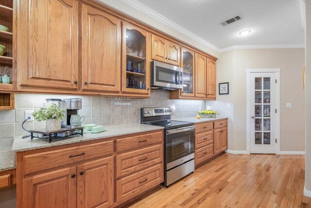 kitchen with backsplash, crown molding, light stone countertops, appliances with stainless steel finishes, and light hardwood / wood-style floors