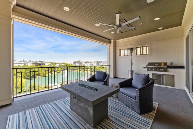 wooden terrace with ceiling fan, area for grilling, an outdoor living space with a fire pit, a water view, and an outdoor kitchen