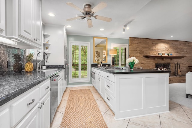 kitchen featuring a brick fireplace, ceiling fan, white cabinetry, ornamental molding, and light tile floors