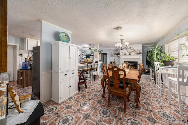 dining space with a chandelier, a textured ceiling, ornamental molding, and a tiled fireplace