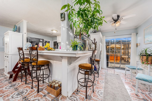 kitchen with white cabinetry, ornamental molding, kitchen peninsula, a breakfast bar, and ceiling fan