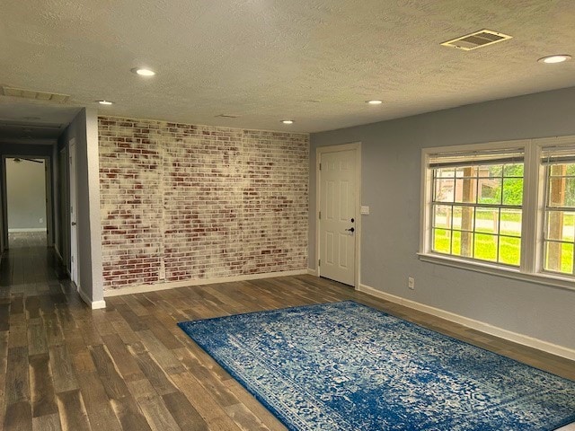 spare room featuring brick wall, a textured ceiling, and dark hardwood / wood-style floors