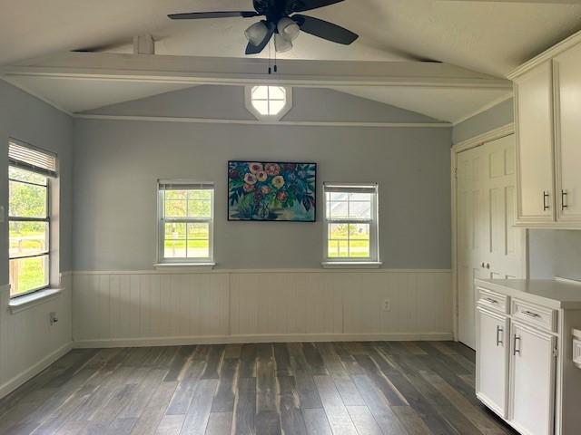 unfurnished dining area featuring dark wood-style floors, ceiling fan, vaulted ceiling, and wainscoting