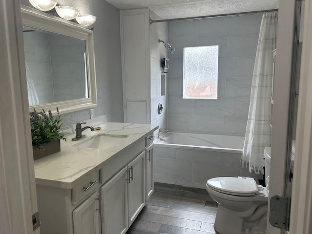 full bathroom featuring toilet, shower / tub combo, hardwood / wood-style floors, vanity, and a textured ceiling