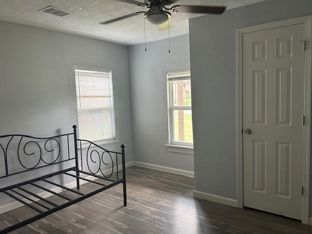 bedroom featuring multiple windows, dark hardwood / wood-style floors, a textured ceiling, and ceiling fan